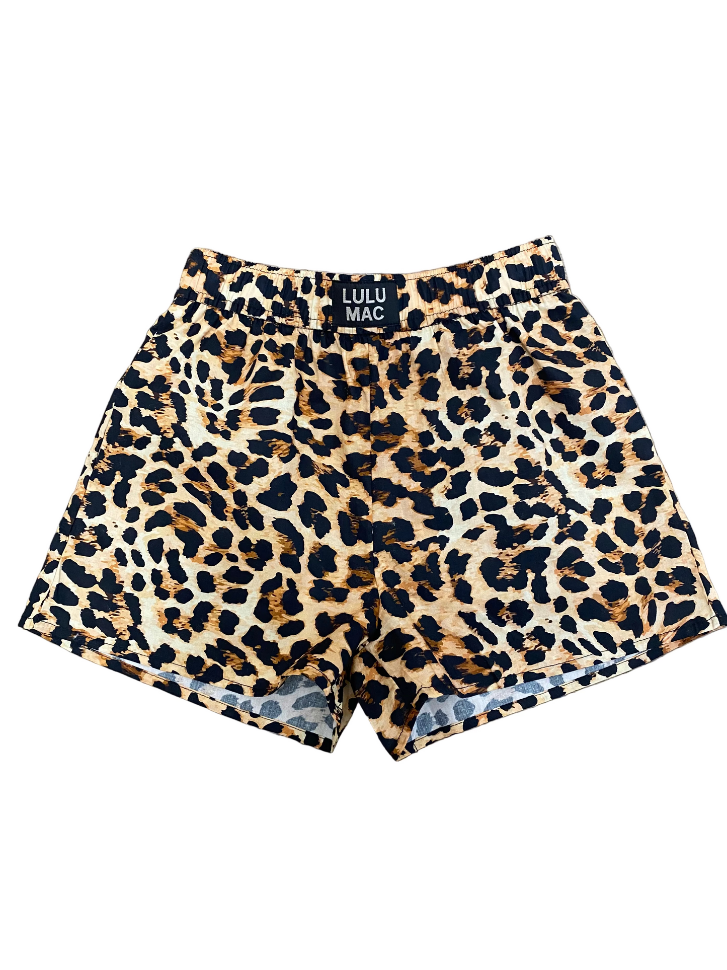 Leopard print shorts with a black waistband label reading 'LULU MAC', laid flat on a brown wood floor.