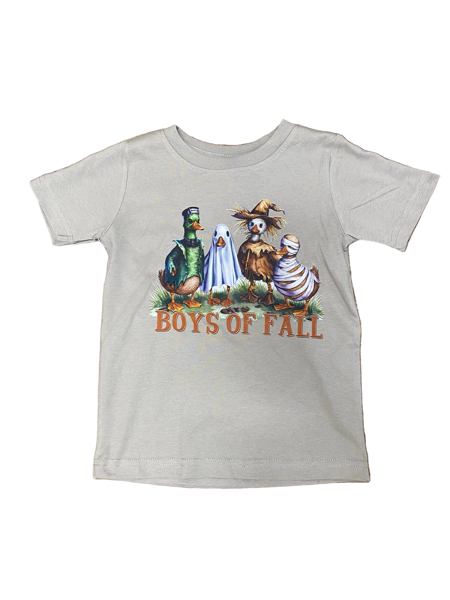 A light gray short-sleeve t-shirt with a 'Boys of Fall' graphic featuring four cartoon characters in autumn costumes, laid flat on a brown wood plank background.