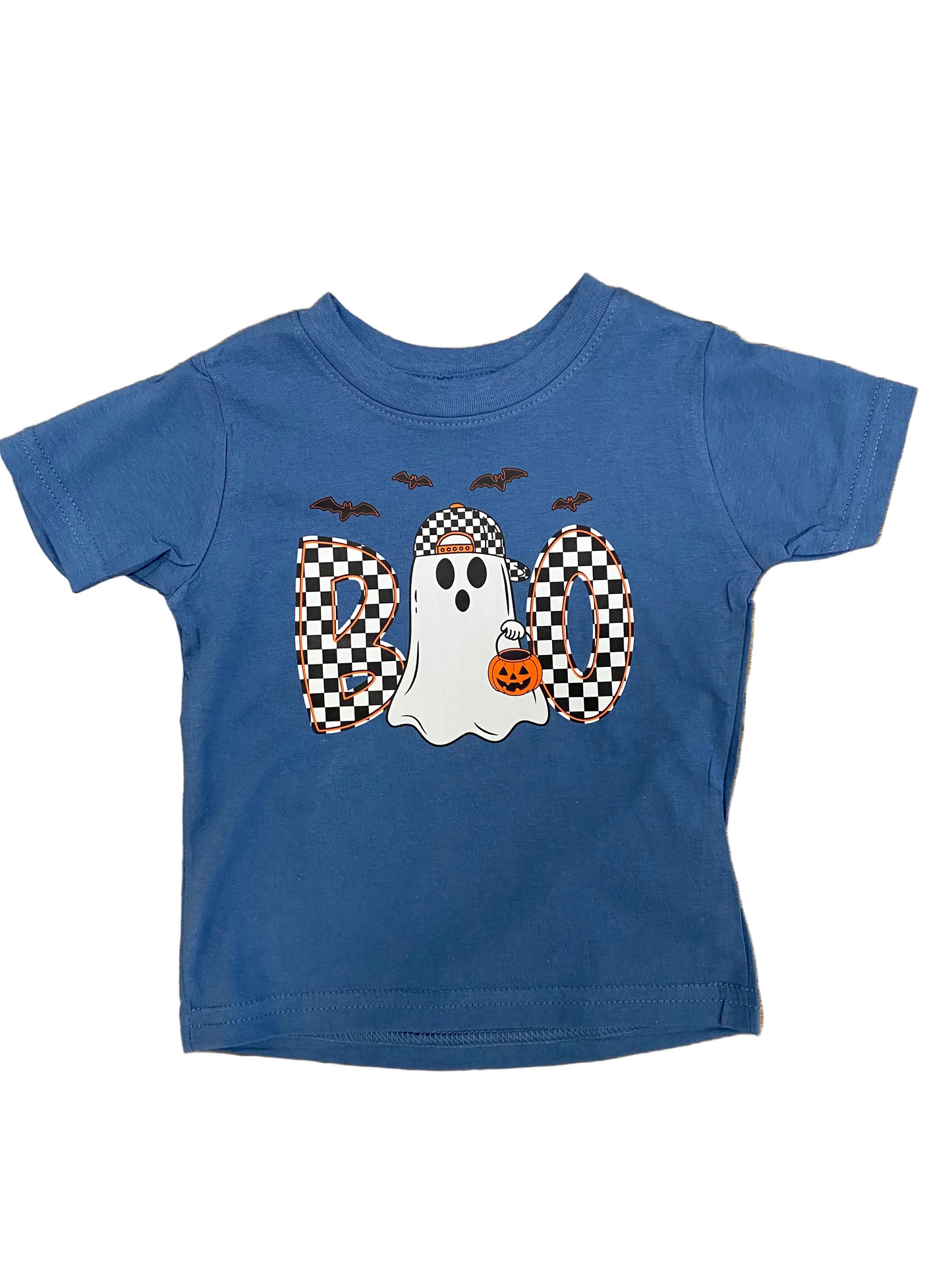 A toddler's blue short-sleeve t-shirt with a Halloween 'BOO' graphic, laid flat on a wooden surface. The graphic features a white ghost wearing a black-and-white checkered hat and holding an orange pumpkin, flanked by checkered 'O' letters, with three black bats above.