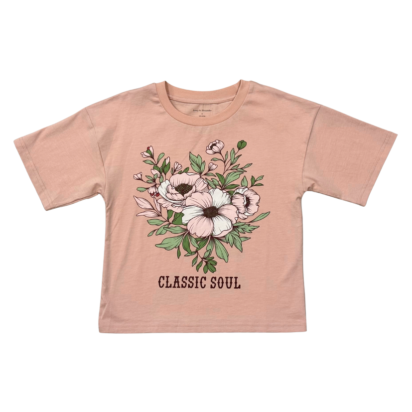 A kids' short-sleeve t-shirt in a dusty peach-pink color, featuring a central floral graphic with pink and white flowers, green leaves, and the text 'CLASSIC SOUL' printed below. The shirt is laid flat against a solid white background.