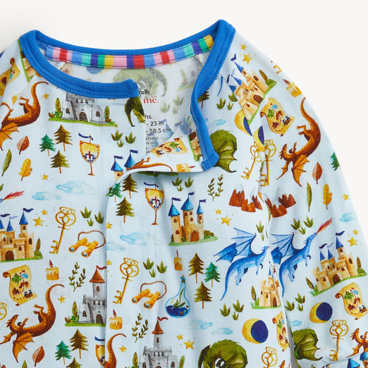 A close-up of a children's long-sleeve pajama top featuring a colorful fantasy castle and dragon print on a light blue base, with a bright blue collar.