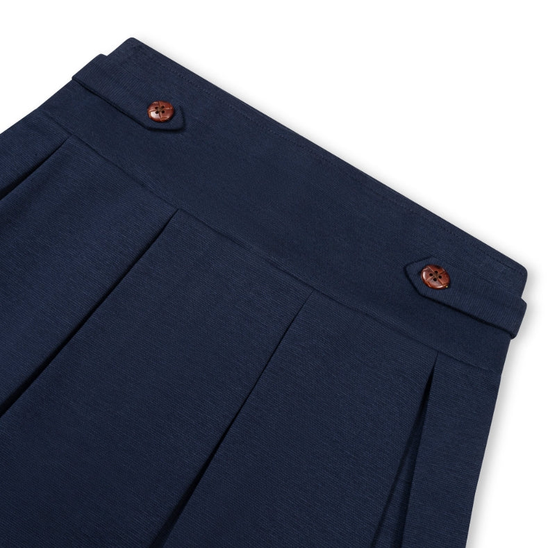 Close-up of navy blue pleated trousers showing the waistband with decorative brown buttons, on a white background.