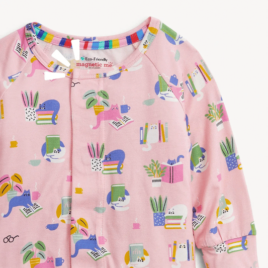 A close-up of a pink long-sleeve baby romper featuring a colorful cartoon print of cats, books, plants, and pencils, with a snap-button front and elastic collar.