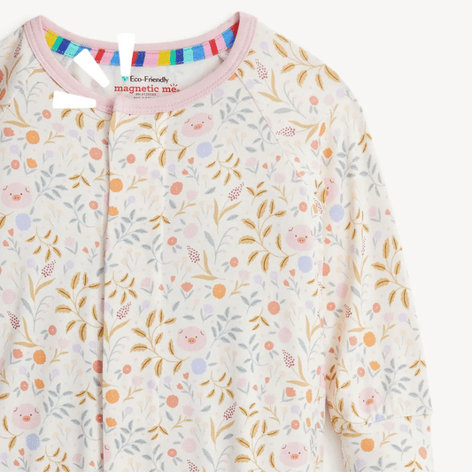 A close-up of a baby long-sleeve top with a colorful pastel floral and leaf print featuring small smiling faces. The garment has a pink collar and a magnetic snap closure at the neckline.