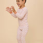 A young boy wearing a long-sleeve, one-piece pajama set with a white base and a repeating peach-orange heart pattern, standing against a solid beige studio background.