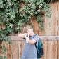 Child holding a toy gun in front of a wooden fence with greenery