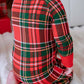 A baby wearing a red and green plaid long-sleeve pajama, shown from the back while sitting on a white fluffy blanket.