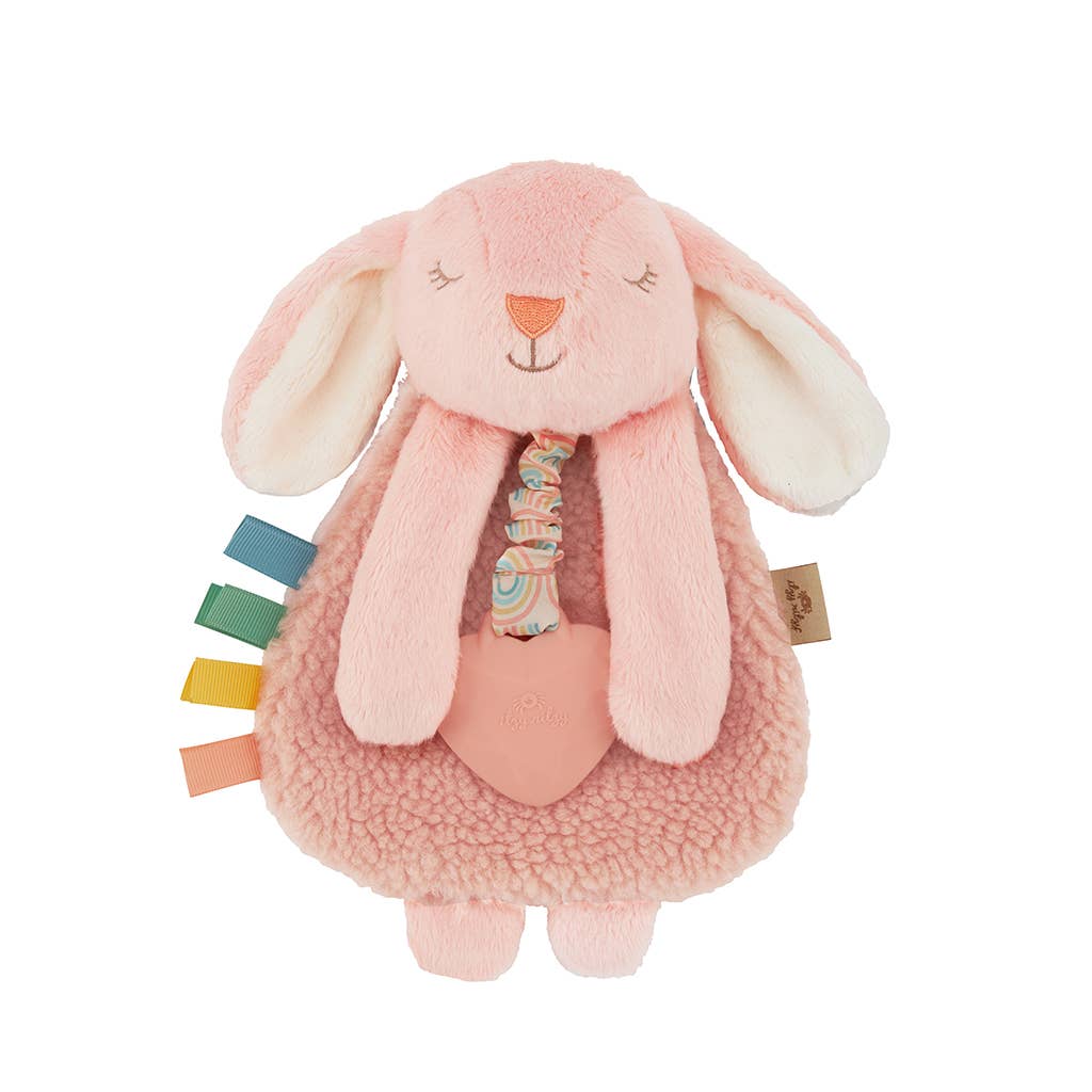 A plush pink bunny with white ears and a multicolored ribbon around its neck, featuring soft sherpa fabric and textured ribbons.