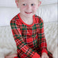 A young boy smiling while wearing a red and green plaid long-sleeve pajama set, sitting on a white textured blanket.