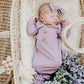 Newborn baby in a purple outfit with a bow