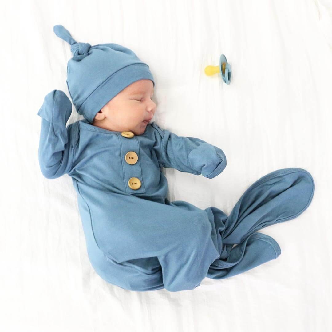 Newborn baby in a blue outfit with button details and matching hat