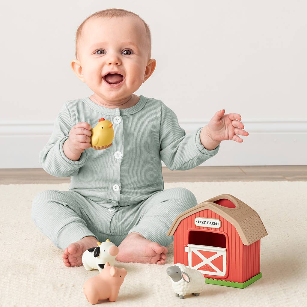 Baby playing with farm-themed toys including a yellow duck, red barn, and pink pig on a light-colored floor.