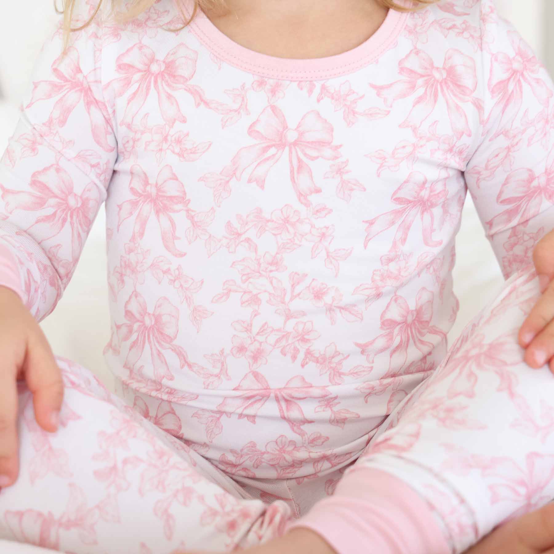 Child wearing a pink and white floral and bow pajama set 