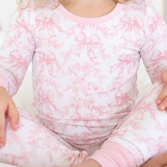 Child wearing a pink and white floral and bow pajama set 
