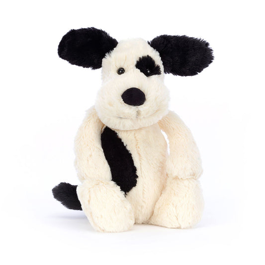 A plush toy depicting a black and cream puppy with a soft body and a black patch on its back. It has a friendly face and a sooty tail.