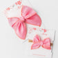 Two pink hair bows on white cards with floral designs.