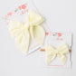 Two yellow hair bows on white cards with floral designs 