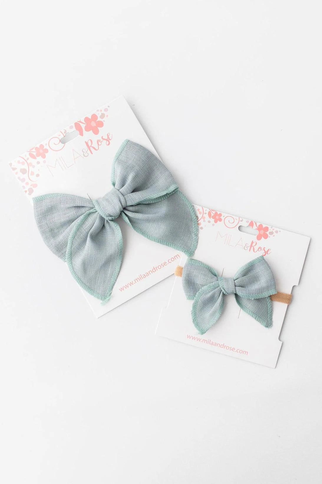 Two sage hair bows on white cards with floral designs.