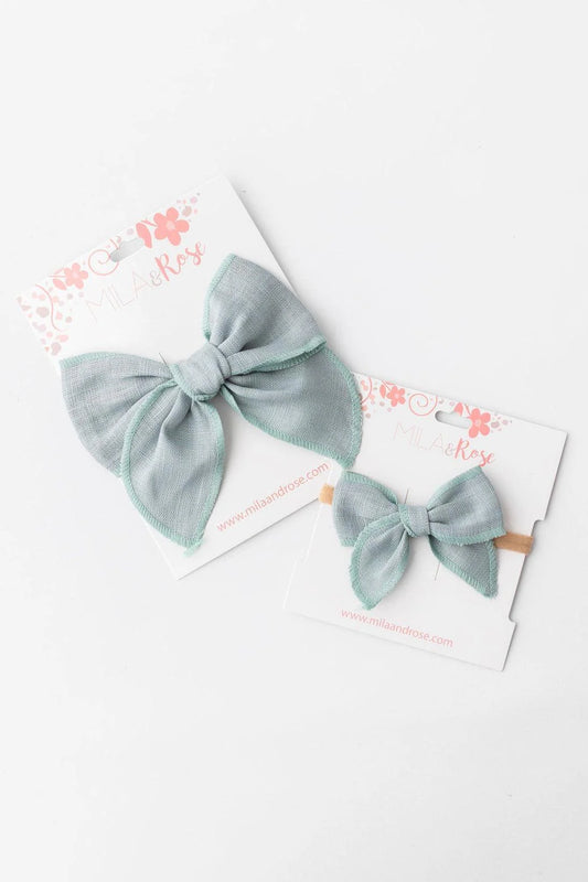 Two sage hair bows on white cards with floral designs.