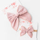 Pink bow headbands on a white card with floral design
