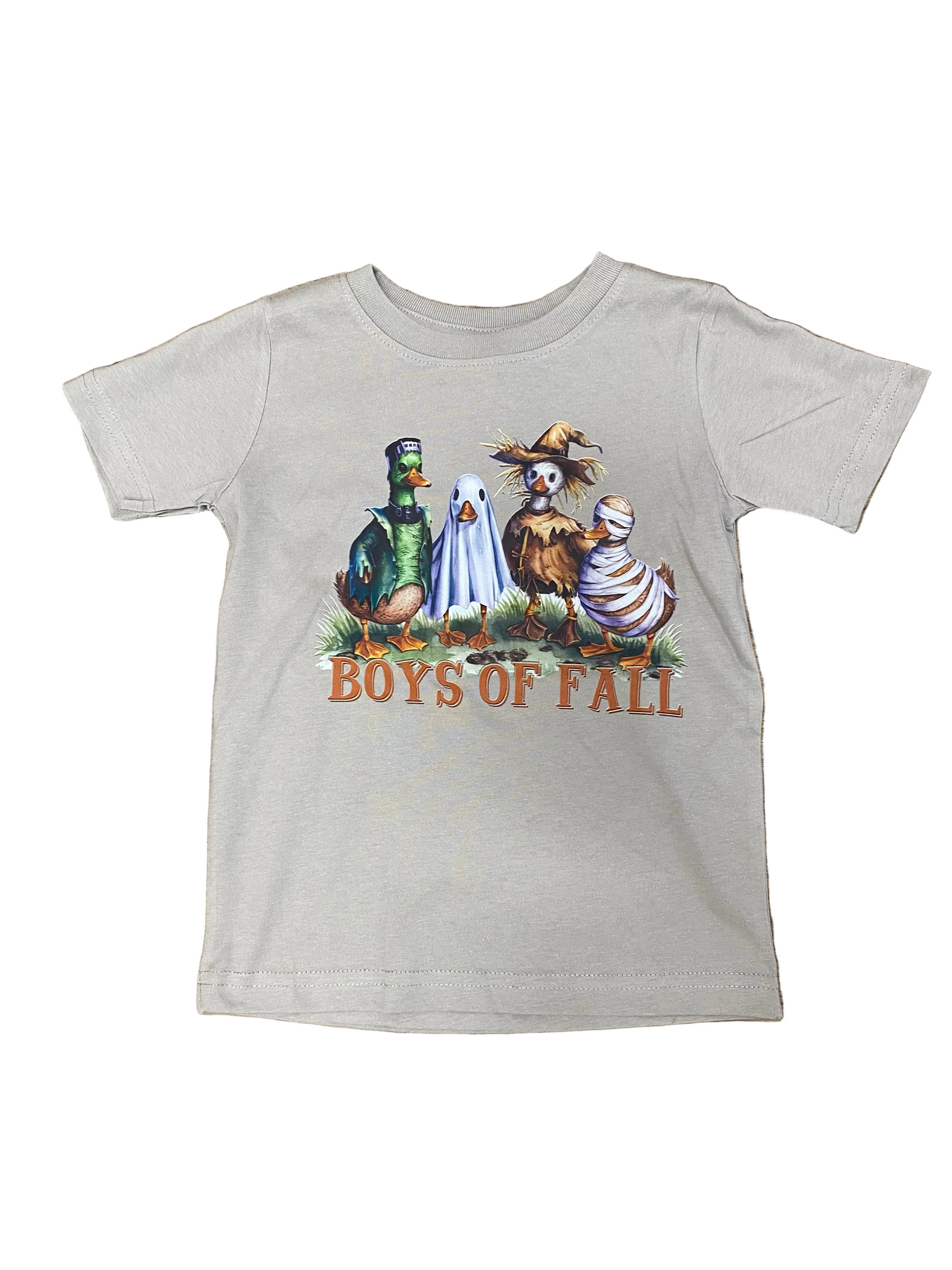 A light gray short-sleeve t-shirt with a 'Boys of Fall' graphic featuring four cartoon characters in autumn costumes, laid flat on a brown wood plank background.