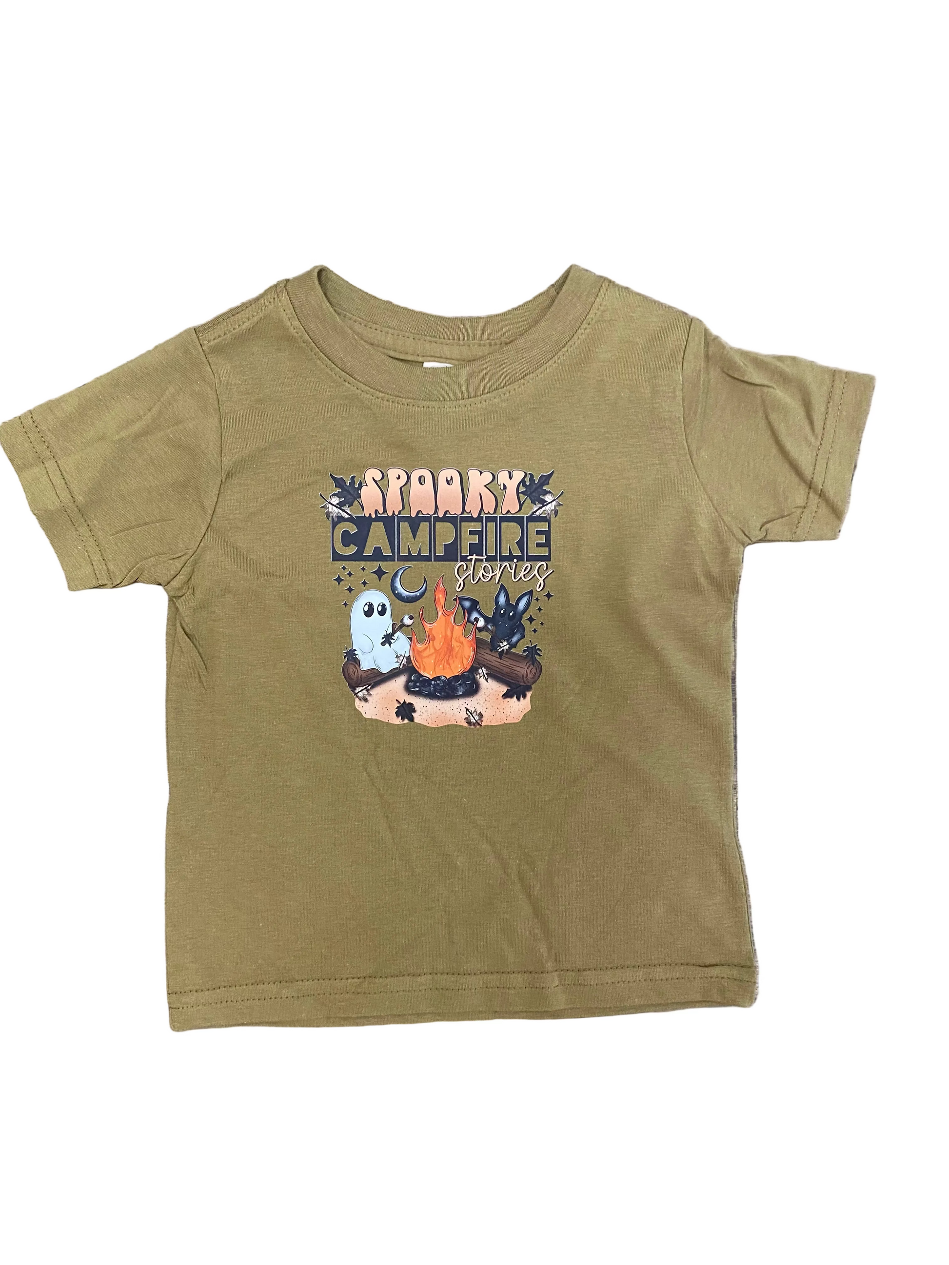 A toddler's olive green short-sleeve t-shirt with a 'Spooky Campfire Stories' graphic, laid flat on a brown wood-grain surface.