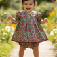Child in a floral dress standing on a path with flowers and greenery in the background