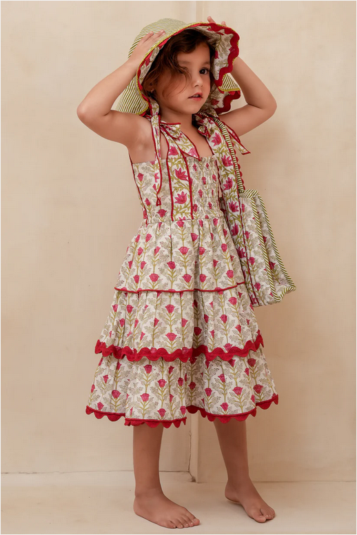 Young girl wearing a floral dress and sun hat against a beige background