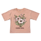 A kids' short-sleeve t-shirt in a dusty peach-pink color, featuring a central floral graphic with pink and white flowers, green leaves, and the text 'CLASSIC SOUL' printed below. The shirt is laid flat against a solid white background.