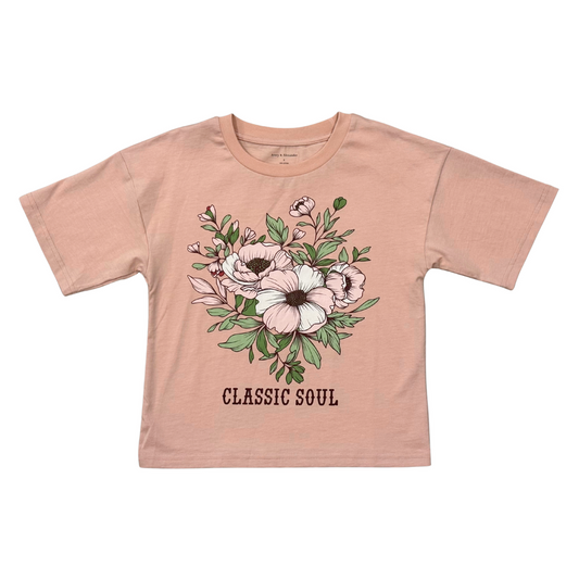 A kids' short-sleeve t-shirt in a dusty peach-pink color, featuring a central floral graphic with pink and white flowers, green leaves, and the text 'CLASSIC SOUL' printed below. The shirt is laid flat against a solid white background.