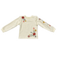 An off-white long-sleeve top with ruffled shoulders and colorful floral embroidery on the chest and sleeve, displayed flat against a white background.