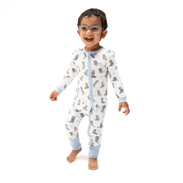 A smiling toddler wearing a light blue and white long-sleeve footless pajama suit with a cartoon animal print, standing against a solid white background.