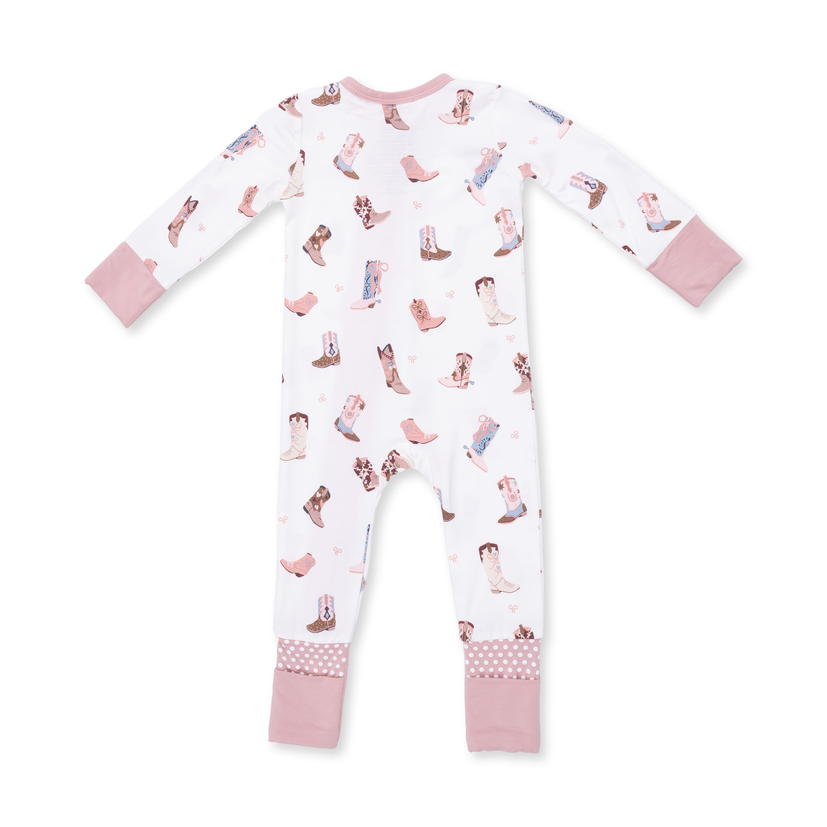 A baby long-sleeve footless pajama romper in white with a pink and brown cowboy boot print, featuring solid pink cuffs and patterned pink cuffs on the legs.