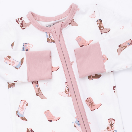 A close-up of a baby romper featuring a white base with a pink zipper and trim, decorated with a pattern of brown and pink cowboy boots.