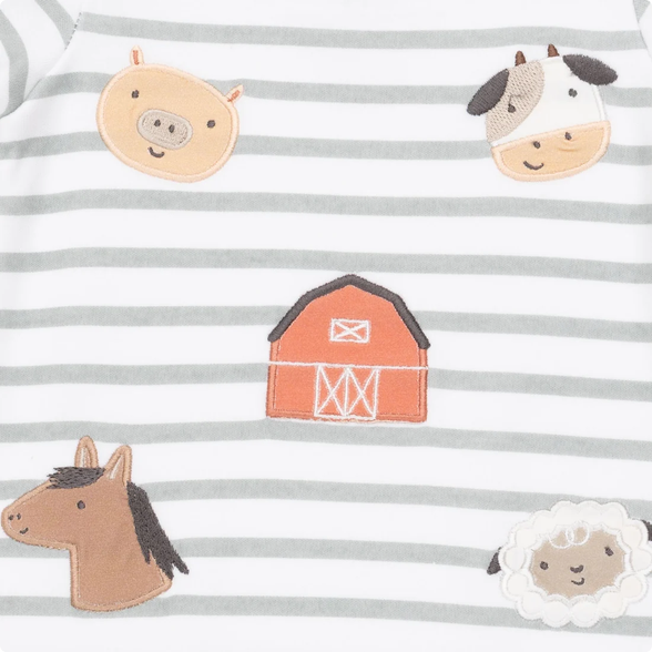 Close-up of a baby garment with horizontal gray and white stripes and embroidered farm-themed motifs including a pig, cow, barn, horse, and sheep.