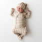 A sleeping newborn baby lying on their back, wearing a beige and white gingham check long-sleeve footed sleeper and matching beanie hat.