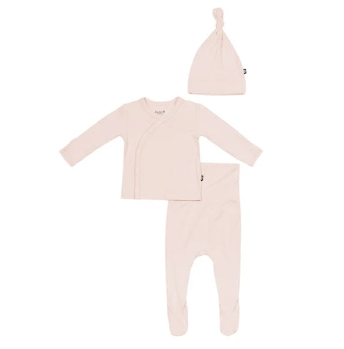 A baby clothing set in a very pale blush pink, including a long-sleeve wrap-style top, matching footed pants, and a knotted beanie hat, laid out on a plain white background.
