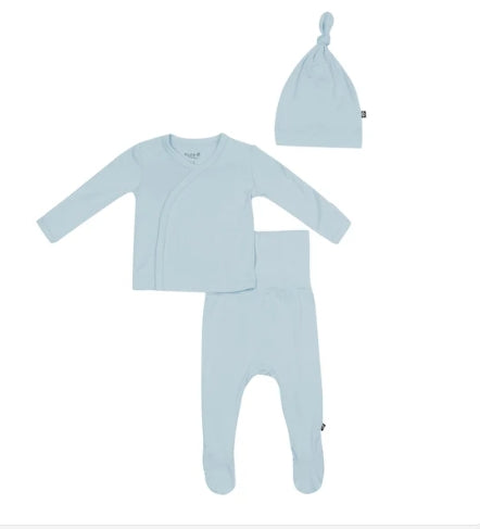 A three-piece baby clothing set in a soft light blue color, including a long-sleeve wrap top, footed pants, and a knotted beanie hat, laid out on a plain white background.