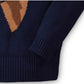 Close-up of a navy blue knit sweater with a brown and tan geometric pattern on the upper chest and ribbed cuffs and hem.