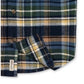 A close-up of a plaid flannel shirt fabric, showing a pattern of navy blue, green, yellow, and white. A small white brand tag is visible on the lower left edge.