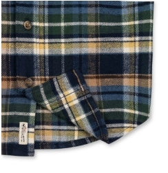 A close-up of a plaid flannel shirt fabric, showing a pattern of navy blue, green, yellow, and white. A small white brand tag is visible on the lower left edge.