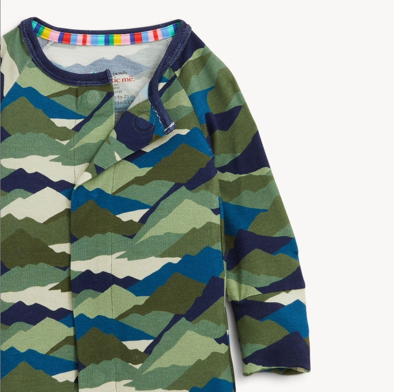 A close-up of a children's long-sleeve top with a mountain-wave camouflage pattern in shades of green, blue, navy, and beige. The garment features a dark navy collar with a colorful striped inner trim and a small brand label visible inside the neckline.
