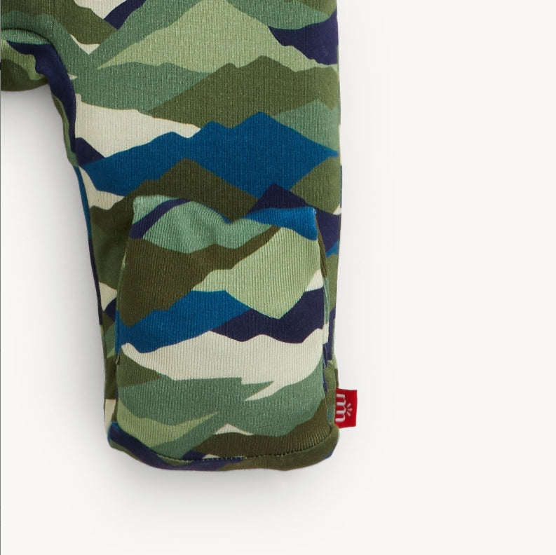 Close-up of a sleeve or cuff with a mountain-patterned knit fabric in green, blue, olive, and cream, featuring a small red brand tag.