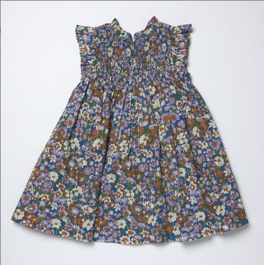 A sleeveless smocked dress with a dense multicolor floral print, featuring ruffled shoulder details and a gathered skirt, laid flat against a light gray background.