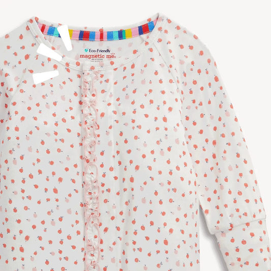 A close-up of a children's long-sleeve top with a white base, small scattered pink and red strawberry print, and a ruffled front placket. The inner neck label reads Eco-Friendly magnetic me.