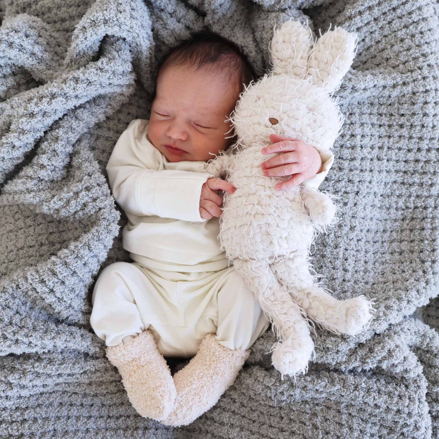 Newborn baby holding a plush bunny toy on a textured blanket