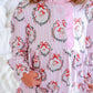 A close-up of a child wearing a pink long-sleeve pajama top with a festive Santa Claus wreath pattern, featuring ruffled trim and a button placket.
