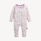 A baby long-sleeve footless one-piece jumpsuit in light pink, featuring an all-over print of illustrated cosmetic bottles and jars in pastel colors. The jumpsuit has a colorful striped inner collar and a small red tag on the lower leg, photographed against a solid off-white background.