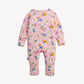 A baby long-sleeve footless one-piece jumpsuit in light pink, featuring an all-over colorful cartoon print of unicorns, books, plants, and gift boxes, shown against a plain off-white background.