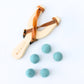 Wooden slingshot with leather straps and blue felt balls on a white background